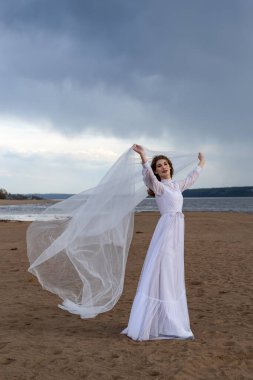 Nehir kıyısında beyaz elbiseli mutlu genç kız. Bulutlardaki fırtınalı gökyüzü 