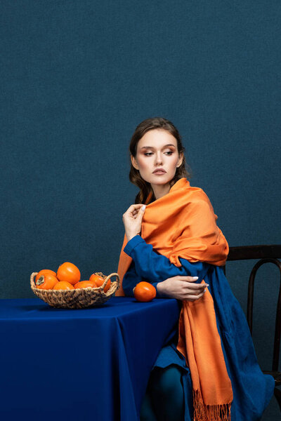 Stylish fashion young woman model, with evening make-up, posing in the studio, holding an exotic fruit in her hand. Photo on a dark blue background