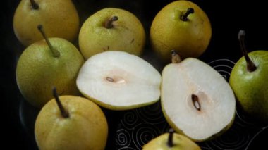 Yeşil armutların üzerine su püskürtülüyor ve dilimlenmiş armutlar bir arada tutuluyor. Taze armutlar ikiye bölünmüş ve kahverengi saplı bütün meyveler bir tabakta bir araya getirilmiş. Besleyici meyve, sağlıklı beslenme, iltihap önleyici özellikler.