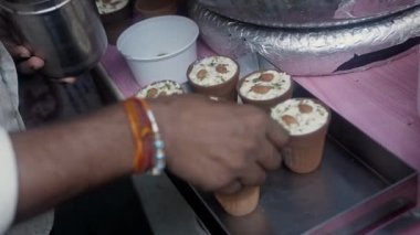 Küçük bir dükkan satıcısı Rabri 'yi kuru meyvelerle süslüyor. Taze yapılmış Rabri, Eski Delhi 'de küçük bir şeker dükkanında büyük bir tabakta duruyordu. Taze, killi çömlekler, geleneksel Hint tatlıları.