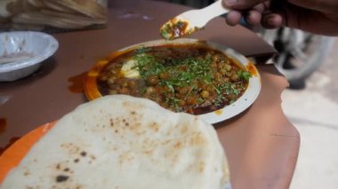 Elinde bir tabak tereyağlı ve dilimlenmiş Dhania olan bir müşteri. Eski Delhi 'de popüler bir yol kenarı tezgahı, Chandni Chowk pazarı lezzetli Kulche Choley satıyor - günlük yemek, Kuzey Hindistan mutfağı, baharatlı Channa