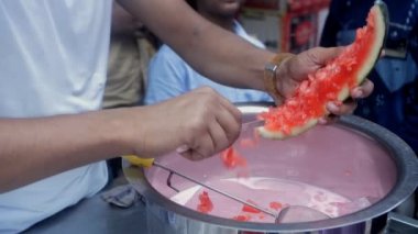 Sulu kırmızı bir karpuz / Tarbooj dilimlenip süte konuyor. Küçük bir meyve suyu köşesinde yerel bir işportacı taze tropikal karpuz püresi yapıyor. Sağlıklı kahvaltı, ferahlatıcı içecek.