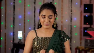 Diwali 'yi kutlamak için elinde parlak bir kil Diya tutan güzel bir kadın. Etnik giysili güzel bir bayan, şenlikli bir arka plana karşı kameraya poz veriyor. Hint kültürü, uğurlu, Hindu festivali.