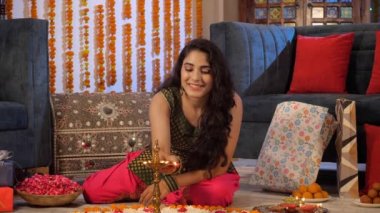 Geleneksel Rangoli 'nin ortasında Diya marka pirinç çakan genç bir kadın. Renkli hediyeler ve geleneksel Hint tatlıları çiçekli arka planda tutulur - Diwali kutlamaları, Hint festivali, festival sezonu