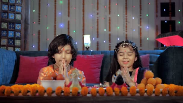 年轻的印度兄弟和他可爱的姐姐在吉祥的节日里做普佳 桌上摆满了传统的印度糖果和灯火通明的Diya Diwali Puja 宗教仪式 印度教节 — 图库视频影像
