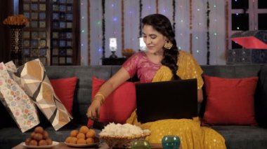 Sari 'li güzel bir bayan video görüşmesinde sohbet ederken Diwali hediyesini gösteriyor. Ev yapımı Hint tatlıları ve çiçek yaprakları bir arada tutuldu. Şenlikli bir arka plan, Hindu festivali, Hint kültürü, ışık festivali.