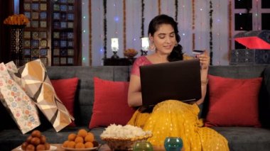 Diwali kutlamaları sırasında evde dizüstü bilgisayarda çalışan çekici bir kadın. Renkli Deepavali hediyeleri ve lezzetli tatlılar bir arada tutuldu - Hindu festivali, uğurlu bir olay, Hint kültürü