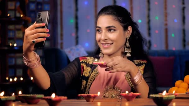 ワックス ディヤを手にしながら自撮りをクリックするインド人女性 明るく燃えるディヤと伝統的なインドのお菓子が一緒に保たれています インドの祭り ディワリのお祝い ヒンズー文化 — ストック動画