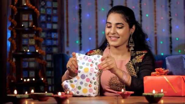 漂亮的女性穿着民族服装兴奋地打开她的Diwali礼物 一个五彩缤纷的礼品盒和燃烧着的油灯在餐桌前欢度佳节 一个印度教的节日 一个印度的灯节 — 图库视频影像