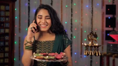 Diwali sırasında telefonda konuşurken ailesine ve arkadaşlarına dua eden genç bir kız. Güzel bir bayan elinde renkli bir tabak Diyas ile evde duruyor - bir Hindu festivali, bir Hint ışık festivali, uğurlu bir olay, birliktelik