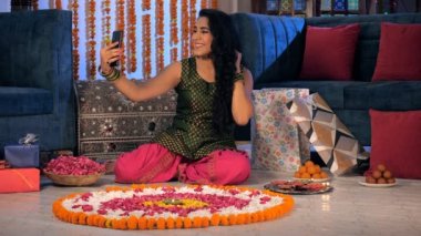 Hint Diwali Festivali 'nde etnik elbise giymiş mutlu bir kadın selfie çekiyor. Geleneksel bir Rangoli, şekerler, hediye kutuları ve çiçek yaprakları bir arada tutulur - şenlik havası, Hint kültürü, dekorasyon