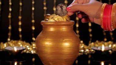 Kalaşta gümüş para saklayan bir kadın. Uğurlu bir olay. İki iyi ışıklandırılmış renkli gaz lambası cam bir masada bir arada tutulur. Diwali dekorasyonu, bir Hindu festivali, şenlik sezonu.