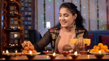 Uğurlu bir günde bir tabak şekeri süsleyen genç bir kadın. Güzel Diyas şenlikli bir arka planda ışıl ışıl yanıyor - Deepavali kutlamaları, Hindu festivali, Hint kültürü