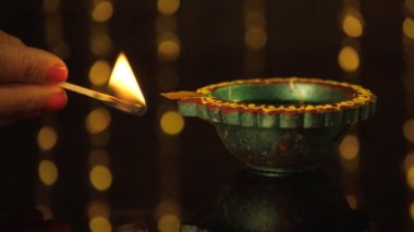 Hayırlı bir günde bir tasarımcı Diya 'yı kibritle yakmak. İyi ışıklandırılmış bir gaz lambası cam bir masada tutuluyor Diwali hazırlıkları, bir Hindu festivali, karanlığı dağıtmak, iyi şans ve barış.