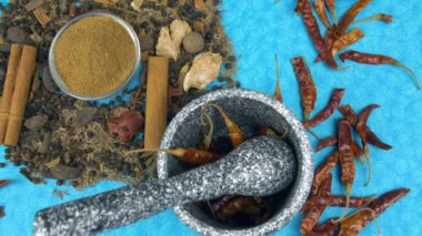 Bir kase Garam Masala tozu diğer Hint baharatlarının yanına konur. Bir kaç kurutulmuş kırmızı biberli havan topu mavi hasırlı bir masada tutulur. Yemek hazırlama, öğütme, tatlandırıcı.