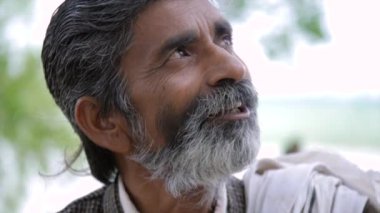 Gri siyah saçlı ve sakallı Hintli Hindu erkek. Yüzü buruşuk, gülümseyen ve konuşan yaşlı bir adam.