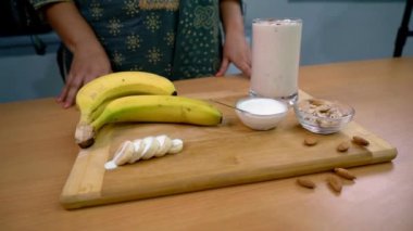 Mutfak tezgahında sağlıklı bir sabah kahvaltısı, sağlıklı beslenme. Dilimlenmiş muz, bir kase krema, badem ve bir bardak milkshake. Protein zengini yemekler.