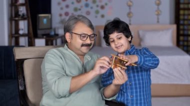 Sevimli bir çocuk ve büyükbabası ahşap bir uçakla oynuyorlar. Genç bir torun büyükbabasıyla evde vakit geçiriyor. Aile bağı, boş zaman, yaz tatili, aile zamanı, Hint ailesi.