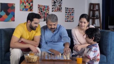 Gri saçlı yaşlı bir adam ve genç oğlu birlikte satranç oynuyorlar. Farklı nesillerin aile üyeleri oturma odasında birlikte oturuyorlar. Boş zaman, aile bağı, büyük aile.