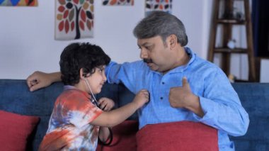 Steteskoplu sıradan kıyafetler giymiş küçük bir çocuk dedesinin kalp atışlarını kontrol ediyor. Sevecen bir büyükbaba ve torunu oturma odasında boş zaman aktivitesi yapıyorlar. Sağlık ve sağlık, iyi büyükbaba, rol yapma, ebeveynlik, mutlu bir hayat....