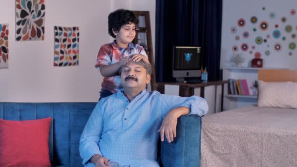 愛情のある孫が老人の家で頭をマッサージしている 疲れとストレスカジュアルな服で快適なソファの上に座っている老人 健康と医療 頭痛の種 インドの家族の絆 — ストック動画