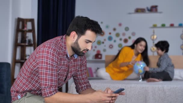 インドの核家族 幸せな父親と教育を受けた母親と彼女の愛らしい息子 リビングルームでリラックスしながら携帯電話で髭を生やした若者 電子機器 現代的な技術 忙しいライフスタイル — ストック動画