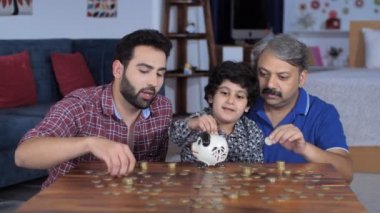 Olgun yaşlı bir adam ve sevimli torunu kumbaraya seve seve bozuk para koyarlar. Oturma odasında boş zaman aktivitesi yapan genç bir baba, oğul ve büyükbaba - mutlu bir çocukluk, aile bağı, birikim, finansal eğitim 