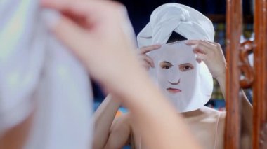Yüzüne maske takan mutlu bir Hintli kadın ve evinde su takviyesi, yüz maskesi. Kolsuz bluz giyen çekici bir kadın cildini tedavi ediyor. Güzellik ve sağlık hizmetleri.