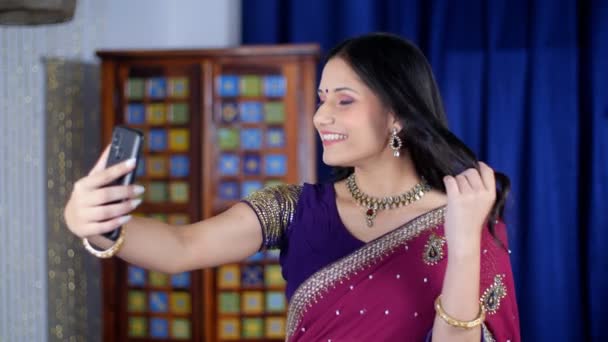 エレガントな服装をしたインド人女性がビデオ通話中に手を振っていた 自宅でスマートフォンを使用して伝統的なサリのかなりの女性 遠隔通信 会議コール 現代的な技術 — ストック動画