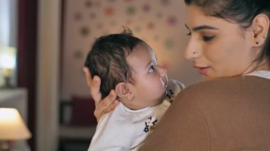 Sevecen bir Hintli anne yeni doğmuş bebeğini kollarında tutuyor. Oturma odasında otururken sevimli bir bebeğe sarılıp öpen sıradan elbiseli güzel bir kadın. Bebek bakıcısı, bebek bakıcısı, aşk ve sevgi.
