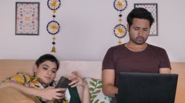 Genç çift kişisel zamanlarında dijital cihazlar kullanıyor. Modern çift, dijital bağımlılık. Çekici bir ev hanımı cep telefonuna bakıyor / bakıyor - boş zaman, elektronik bir cihaz, yoğun bir yaşam tarzı