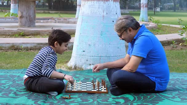 眼鏡をかけた老人が孫とチェスをしている 彼の父親が公園でチェスをしている若い男の子 ボードゲーム 余暇時間 Checkmate — ストック動画
