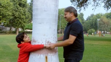 Genç bir çocuk ve yaşlı bir adam bir ağacın arkasında saklanırken birbirlerine sarılıyorlar. Büyükbaba ve tatlı bir torunun parkta birlikte oynaması - boş zaman, aile bağı, mutlu bir çocukluk, eğlenceli bir aktivite
