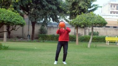 Yakışıklı okul çağındaki bir çocuk parkta tek başına top oynarken eğleniyor. Açık havada gündelik kıyafetlerle oyun oynayan genç bir çocuk. Boş zaman, aktif yaşam tarzı, spor aktiviteleri.
