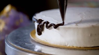 Pasta şefi, kremalı kekin üzerine çikolata sıkıyor. Boru torbasıyla. Doğum günü partisi için beyaz pasta süslemek - çekici, güzel, olay, kutlama