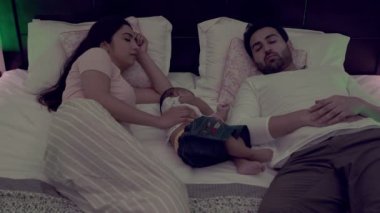 Hintli bir anne geceleri uyurken sevimli bebeğine sarılıyor. Genç ebeveynler tatlı oğluyla rahat bir yatakta yatarlar. Aile bağları daha hızlı uyumana yardım eder. Rahatlamana, yorgun ebeveynler, yeni ebeveynler, ebeveynlik. 
