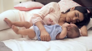 Yatakta tek başına oynayan sevimli, sevimli bir kız bebek. Uyurken küçük kızına sarılan yorgun bir Hintli anne - anne-çocuk bağı, iyi bir uyku, mutlu bir çocukluk