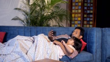 Genç bir çocuk ve baba geceleri online video izliyorlar. Ebeveynlik, bekar baba-oğul yakınlaşması. Küçük bir çocuk ve yakışıklı bir adam oturma odasında rahat bir kanepede dinleniyorlar. Ebeveyn-çocuk bağı, mutlu bir çocukluk.