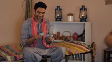 Kurta Pijamasında mutlu bir Hintli çiftçi geçen ayki maaşını hesaplıyor. Maaş, tarım geliri. Bir Chaarpai bankasında otururken elinde yüz, iki yüz, beş yüz rupi tutan neşeli bir köylü - bankacılık ve finans, tasarruf