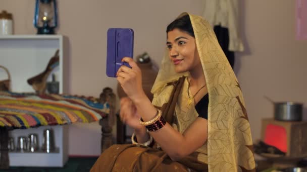 印刷物を着たインドの伝統的な女性Sareeは 額にBindiを適用します 農村インド 進歩的な農家 小さな鏡の前で準備をする美しい村の女性 — ストック動画