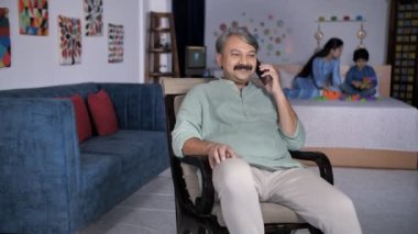 Yaşlı bir adam, gelini oğluyla oynarken cep telefonuyla konuşuyor. Farklı nesillerin aile fertleri. Büyükbaba sallanan sandalyede oturuyor, telefonla konuşuyor, meşgul oluyor, ortak bir aile kuruyor. 