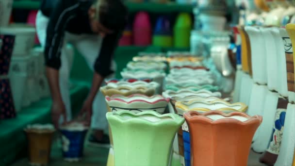 一个年轻人把漂亮的瓷壶一起放在托儿所里 销售用的不同颜色 不同色调的空装饰种植盆 兵马俑 — 图库视频影像