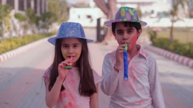 Renkli şapkalar takan Hintli çocuklar birlikte düdük çalarken eğleniyorlar. Holi kutlamaları, çocukluk oyunları, boş zaman. Holi 'yi kutlayan neşeli kardeşler. Aile bağı, küçük kardeş, Hindu festivali.