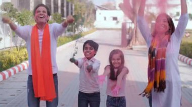 Çekici bir çift ve çocukları Holi oynarken havaya boya fırlatıyorlar. Boş zaman, kuru renkler, organik Gulal. Neşeli bir Hintli çift çocuklarıyla Holi 'de dans ediyor. Keyif, şenlik havası, birliktelik ve bağ.