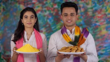 Holi 'de bir tabak sarı Gulal ve geleneksel Gujia tabağı olan Hintli gençler. Uğurlu bir olay, Hint renk festivali, Kızılderili kardeşler. Neşeli bir kız ve festival sırasında kameraya poz veren beyaz Kurta giyen yakışıklı bir adam....