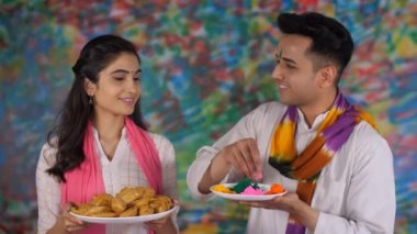 Holi festivalini alnına Gulal Tilak 'ı koyarak kutlayan iki genç. Elinde geleneksel Gujia tabağı olan beyaz bir Kurti giyen neşeli bir kız. Bir Hint renk festivali, bir bahar festivali, uğurlu bir olay.