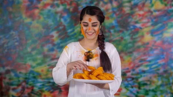 伝統的なグジヤ インドの甘い 甘い珍味 おいしい料理 を持つハッピーホリを人々に望む編組の髪を持つかなりインドの女の子 インドの色の祭りを祝う白いクルティの美しい女性 ヒンズー教の祭り — ストック動画