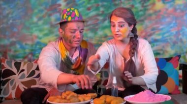 Holi festivalinde ellerini dezenfekte eden yakışıklı bir adam ve güzel bir bayan - Covid-19 yaşam tarzı, temizlik ve hijyen, dezenfektan. Genç bir çift Hint renk festivalini lezzetli yemek ve tatlılarla kutluyor. Bayram sezonu, atıştırmalık....