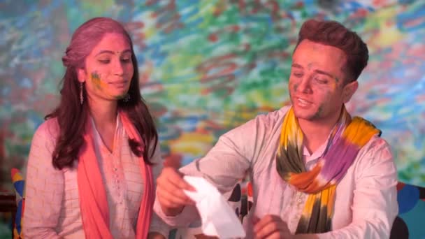 ティッシュペーパーを使用して彼の友人のかなりの顔にグルを拭く男 ホリ祭りのお祝い 有機色 若いカップルは インドの色の祭りの間に家で一緒に時間を過ごす ヒンズー教の祭り お祝いの気分 — ストック動画