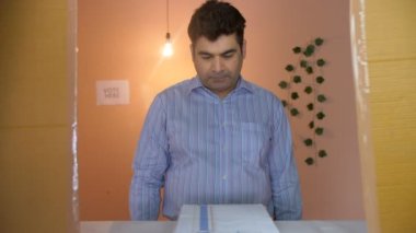 Şehir merkezinden neşeli, orta yaşlı bir adam oy kullanma kabininde oy veriyor. Belediye seçimleri, oy kullanma hakkı, demokratik bir ülke, Hindistan parlamento seçimleri. Gündelik giysiler içinde yakışıklı bir adam oy verdikten sonra olumlu bir jest gösteriyor....